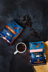 Two bags of Copper Door Coffee Roasters coffee beans with a mug and beans around them